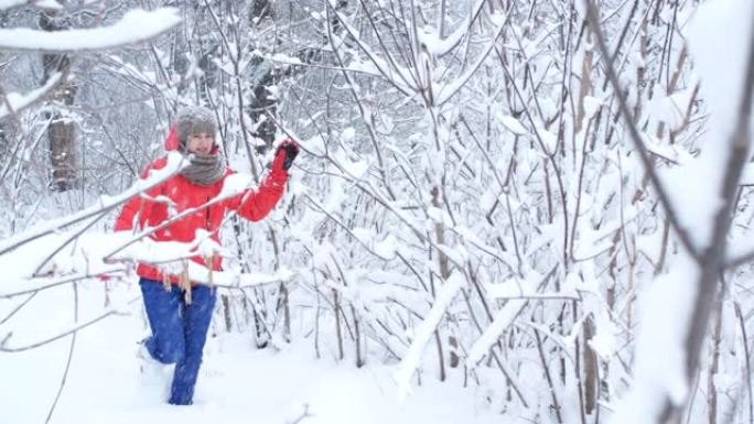 女旅行者跳过白雪覆盖的森林。雪挂在树枝上，一碰就碎了。