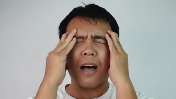 特写严肃的亚洲男人闭上眼睛，擦着头的肖像，在灰色背景上表示沮丧和压力。情感和表达概念。