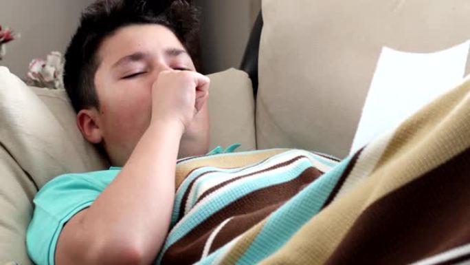 生病的小男孩在毯子覆盖的沙发上咳嗽