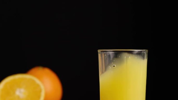 冰块落在黑色背景上的橘子果汁或柠檬水玻璃中。用天然成分准备健康早餐。慢动作。