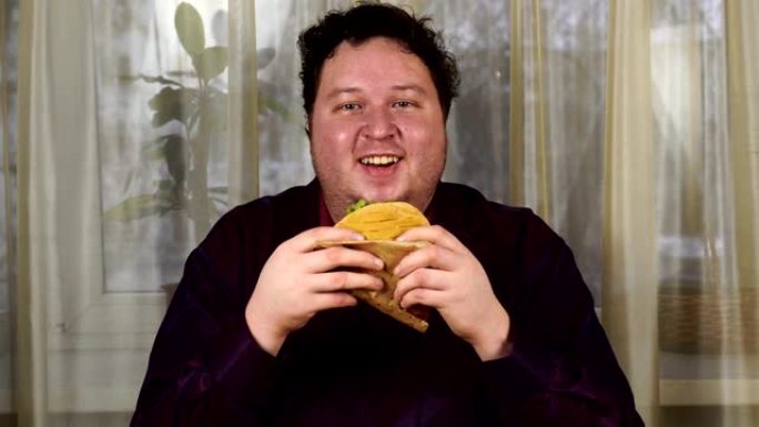 拿着三明治的年轻人。胖子吃快餐。玉米饼不是有益的食物。非常饿的家伙。