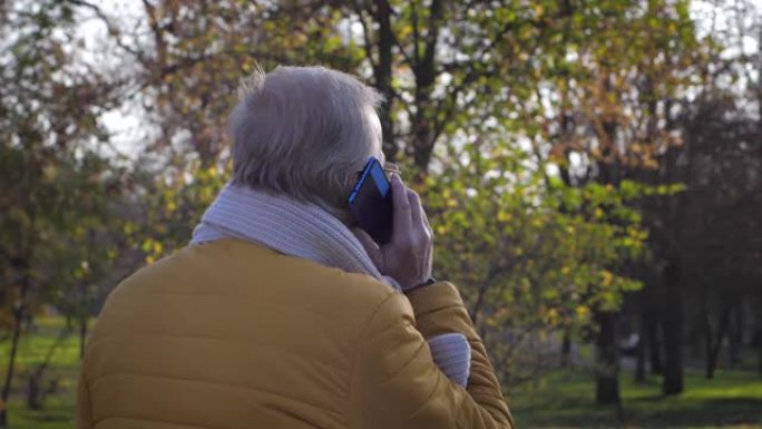 退休人员在秋季公园散步时用手机聊天，现代老年