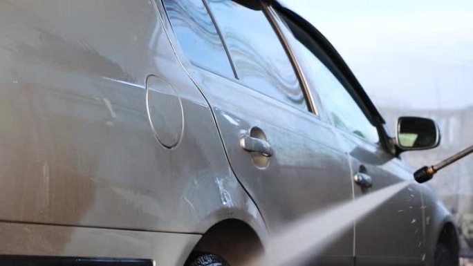 洗车。一名男子在水的压力下洗车并擦玻璃。汽车护理概念