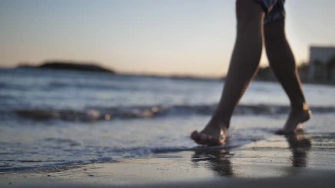 男子在日落时沿着海岸线行走腿特写慢动作