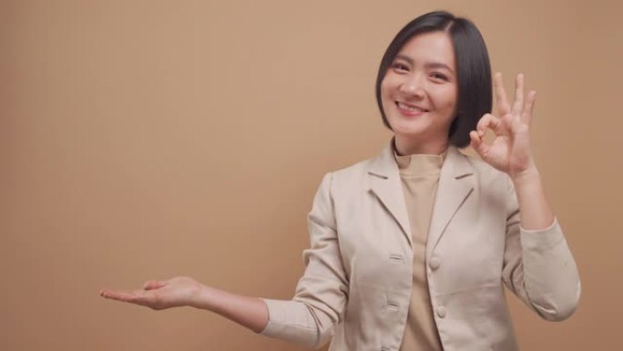 亚洲女商人快乐的微笑用OK手语展示她的手，复制空间隔离在米色背景上。4k视频