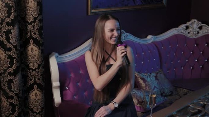 年轻女孩在卡拉ok俱乐部的沙发上对着麦克风唱歌