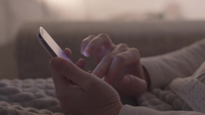 现代概念: 女人的手坐在沙发上的特写镜头，用手指在屏幕上使用智能手机，在现代柔和的光线环境中，没有分