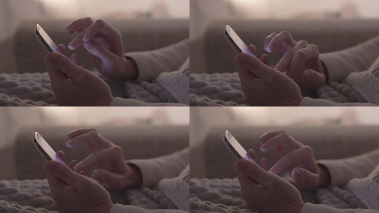 现代概念: 女人的手坐在沙发上的特写镜头，用手指在屏幕上使用智能手机，在现代柔和的光线环境中，没有分
