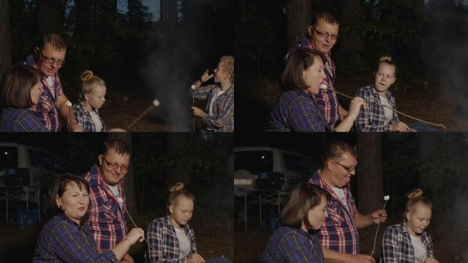 家庭在夏季森林中吃篝火上炸的热棉花糖。旅游家庭在夏季露营中尝试在森林野餐中烤棉花糖。