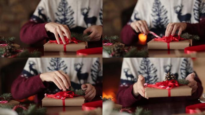 男人的双手在壁炉附近的圣诞节礼物上系蝴蝶结，包装盒，用杉木树枝，圆锥体，藤糖装饰在桌子上，然后向相机