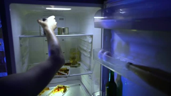 在冰箱里找食物的人。该名男子打开冰箱，将罐头食品放入其中。