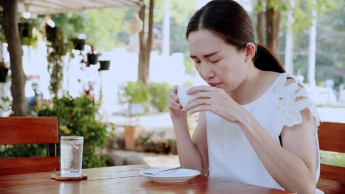 亚洲女性坐在咖啡店的花园里喝热黑咖啡或热茶。在一天的早晨将有助于恢复身体，并对消化系统的健康有良好的