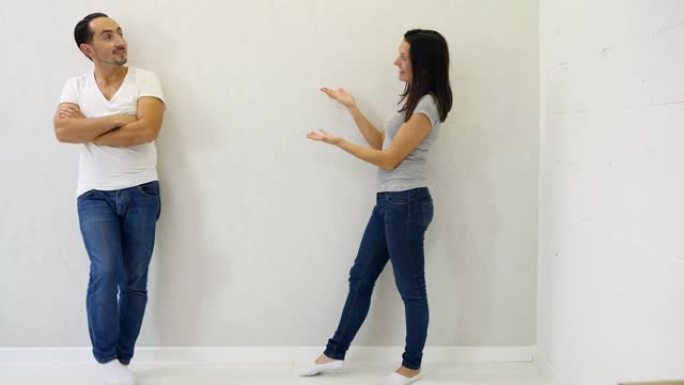 迷人的男人和女人站在白色背景的不同侧面，指着他们之间的复制空间，然后竖起大拇指，微笑着。
