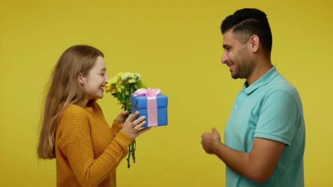 英俊的黑发男人给美丽的姜女友礼物和鲜花，她饶有兴趣地摇着礼物，男人打手势不