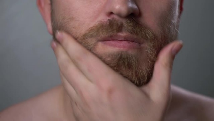 一个年轻人用手触摸他的大胡子和小胡子，特写。
