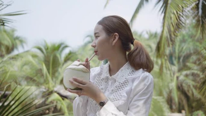 亚洲女人看着大自然，喝椰子水
