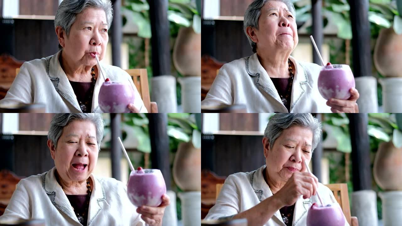 老亚洲老年妇女在餐厅喝浆果奶昔。成熟的退休生活方式