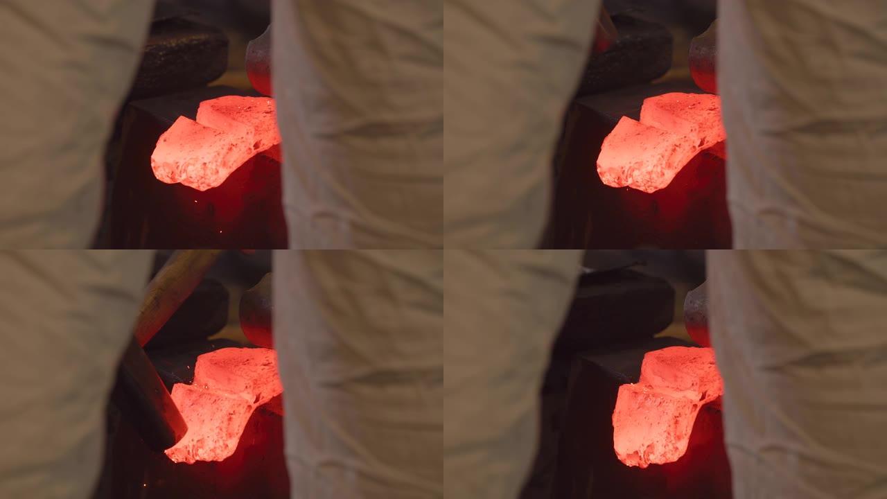 黑色史密斯大师的两腿之间的视图用大锤敲打红色的热锭，以折叠钢材并形成哈蒙。传统的日本锻造方法。日本工