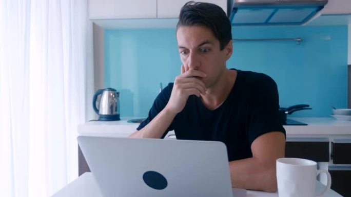 疲惫的年轻人在家厨房里用笔记本电脑工作。一个男人受苦头痛。
