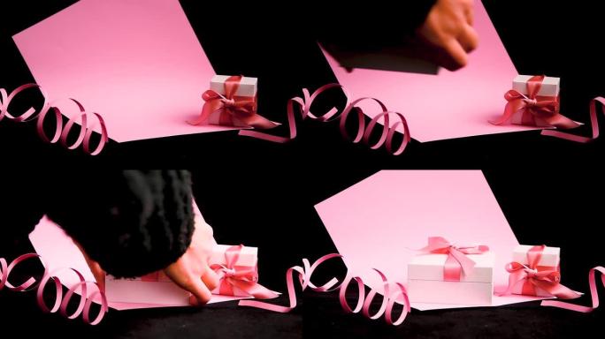 女性手放置礼物盒，粉色和黑色背景上有粉色丝带