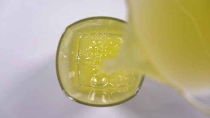 将鲜榨橙汁倒入桌子上的玻璃杯中的俯视图。白色背景上清爽黄色饮料的慢动作