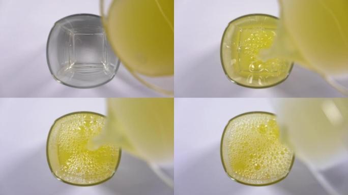 将鲜榨橙汁倒入桌子上的玻璃杯中的俯视图。白色背景上清爽黄色饮料的慢动作