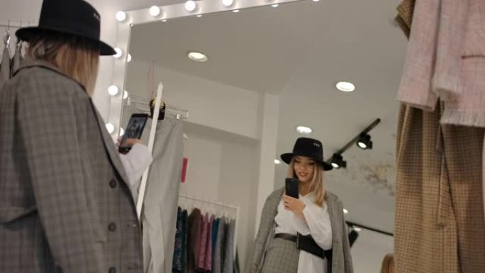 时尚的年轻女子在试衣间对着现代精品店的大镜子自拍