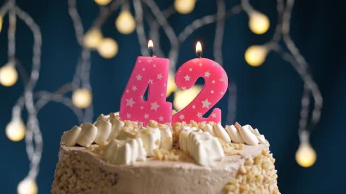 蓝色背景上有42号粉色蜡烛的生日蛋糕。蜡烛着火了。慢动作和特写视图