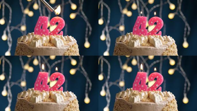 蓝色背景上有42号粉色蜡烛的生日蛋糕。蜡烛着火了。慢动作和特写视图