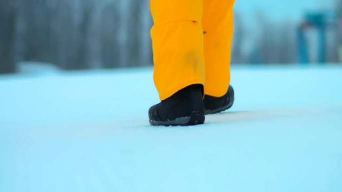 一个人的腿在雪地里行走。脚走在雪道上。后视图。