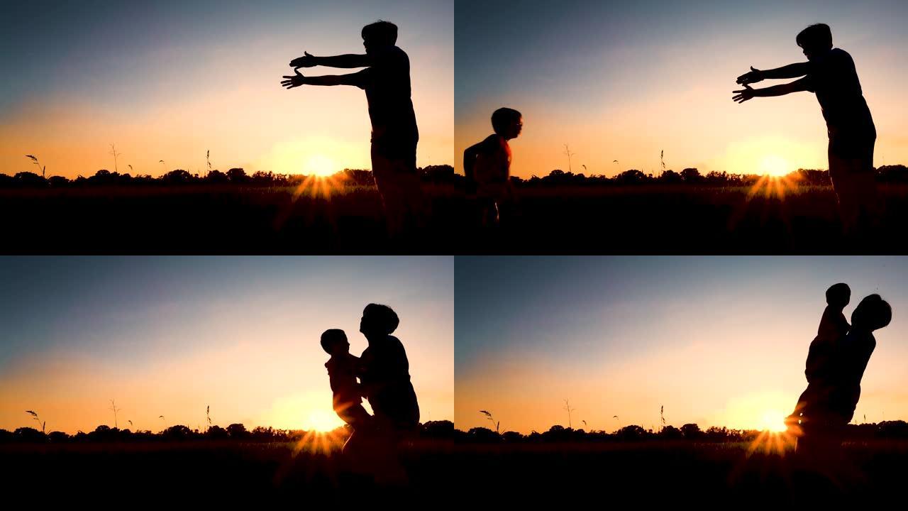 剪影快乐的孩子跑进父亲的怀抱。日落天空背景下的家庭拥抱