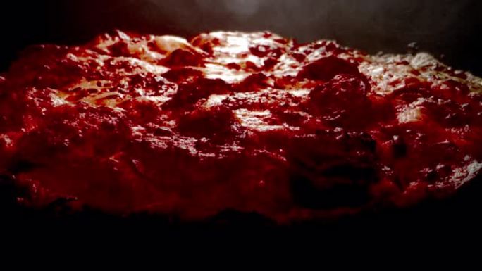 特写广角宏观静态拍摄美味热气腾腾的深盘意大利辣香肠比萨饼新鲜出炉在加热灯下的冷却架上