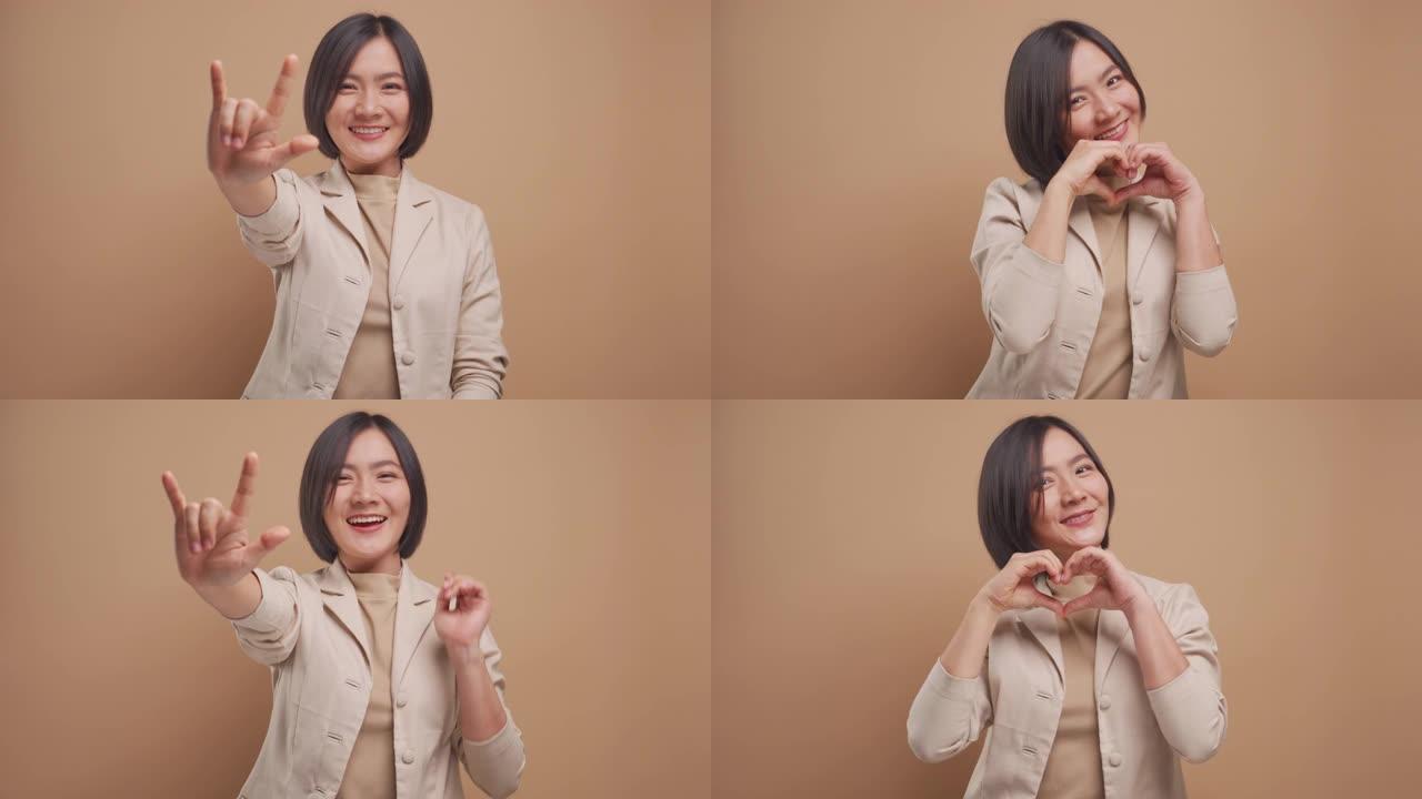 恋爱中的快乐亚洲女商人展示我爱你的手语，看着米色背景上孤立的相机。4k视频