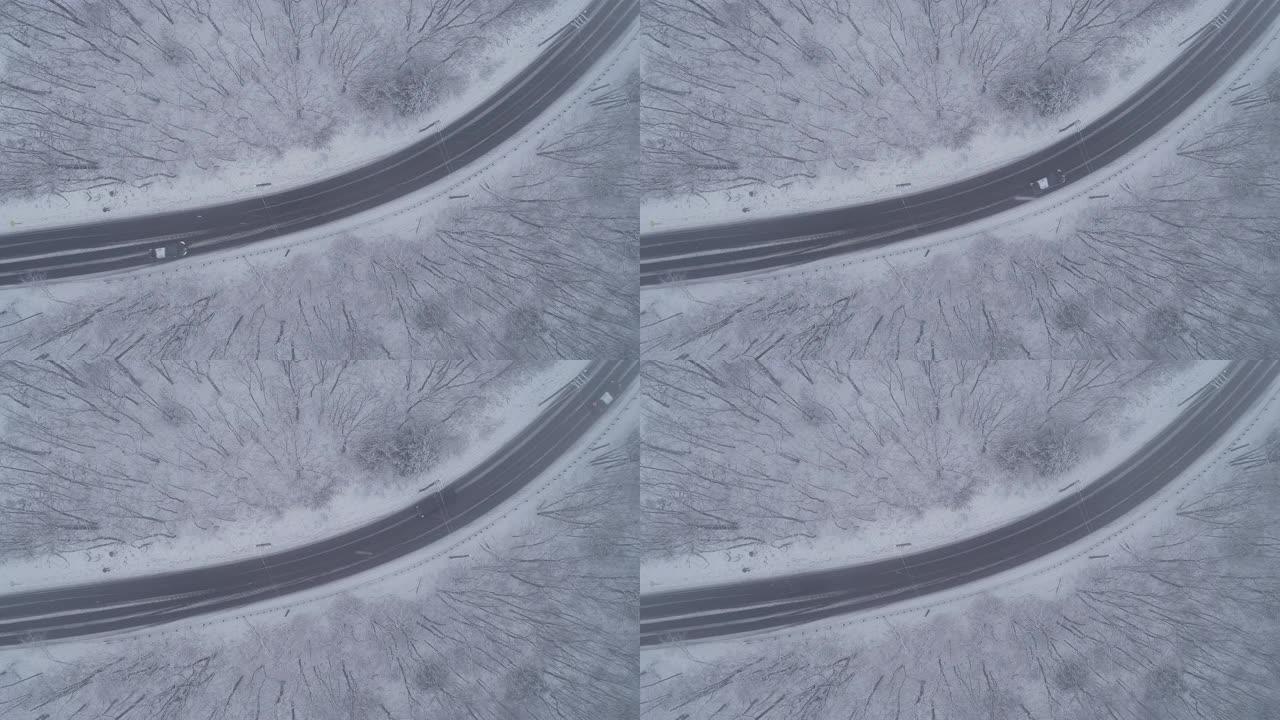 在降雪下，在高速公路弯道上行驶的汽车穿过森林。静态俯视摄像机的无人机航拍视频。