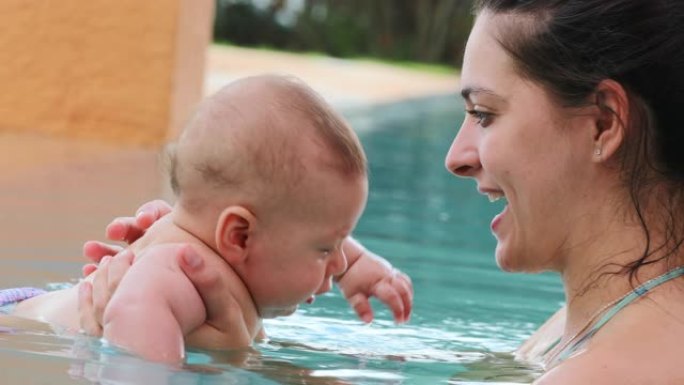母亲抱着婴儿儿子在游泳池里的水互动