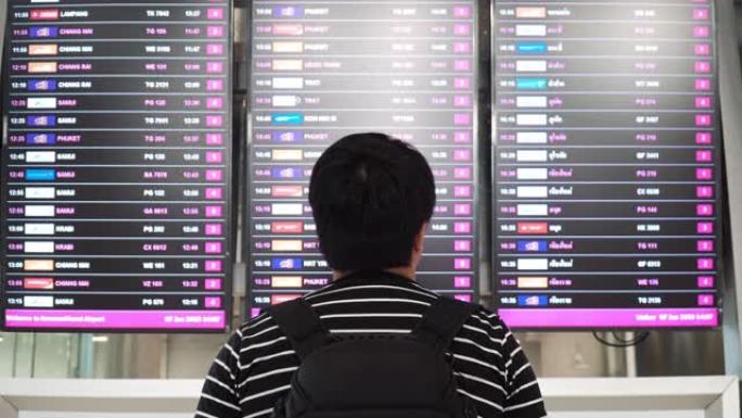 亚洲男子在机场到达离境板寻找登机口。