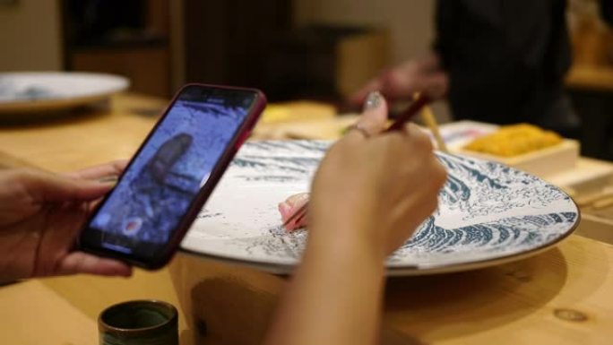 一名妇女在一家日本小餐馆里用智能手机拍摄寿司的照片