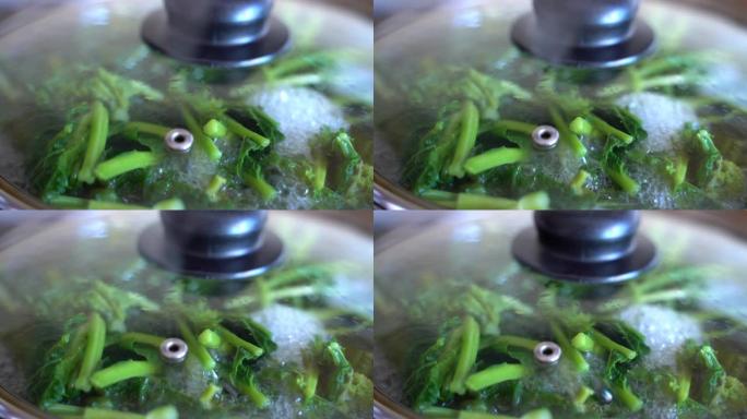 在厨房炉灶上的炊锅中蒸蔬菜，在里面蒸开水和新鲜菠菜。蒸汽和蒸汽概念，素食，健康饮食和饮食概念