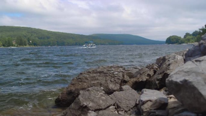 在阴天的夏日，海浪在湖边的岩石上撞击，有浮船