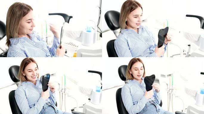 一个微笑的女孩的肖像金发在牙科椅上，手里拿着牙形镜。快乐客户牙科柜