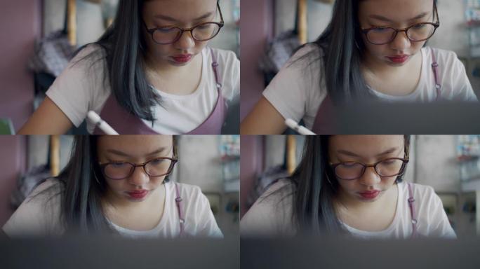 亚洲女商人戴着眼镜思考，在家庭办公室工作，用平板电脑、智能手机和笔记本电脑。写字和画画决心专注于工作