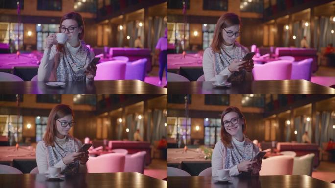 戴着眼镜的美丽微笑女孩的肖像使用智能手机与社交网络上的朋友聊天，在昂贵的体面餐厅放松时喝咖啡