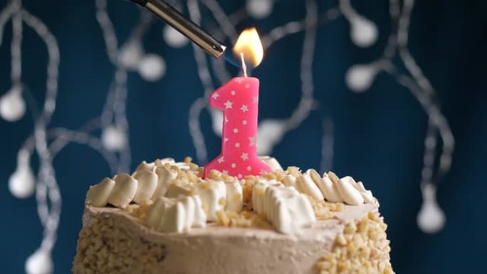 蓝色背景上有1号粉色蜡烛的生日蛋糕。蜡烛着火了。慢动作和特写视图