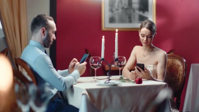 情侣聊天在无聊的浪漫约会期间使用智能手机。红色相机上的中等镜头