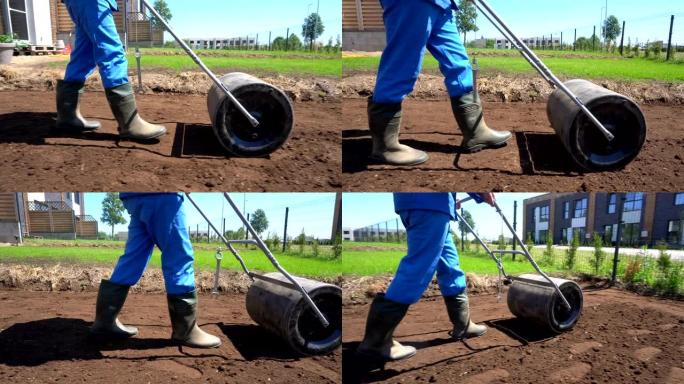 穿着胶靴的工人与土壤压路机一起工作。万向节平行跟随射击