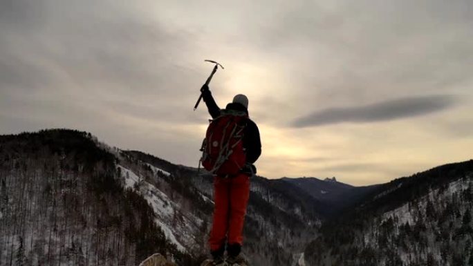 一个年轻的男性登山者站在山顶上，手里拿着一把冰斧的轮廓。