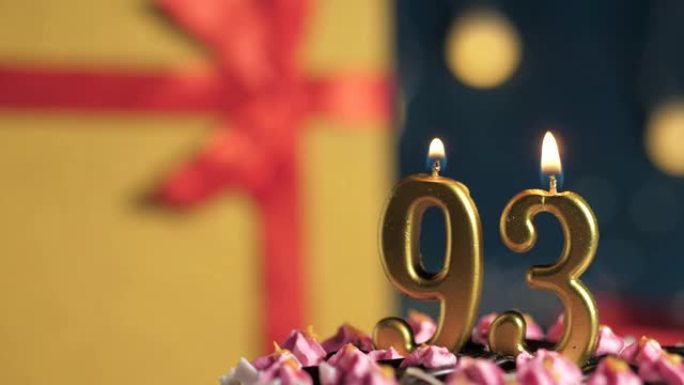 生日蛋糕93号点火器燃烧的金色蜡烛，蓝色背景礼物黄色盒子用红丝带绑起来。特写和慢动作
