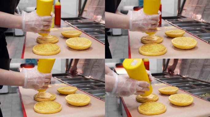 厨师将蛋黄酱脂肪酱倒在带有芝麻的小圆面包上，作为汉堡包特写镜头