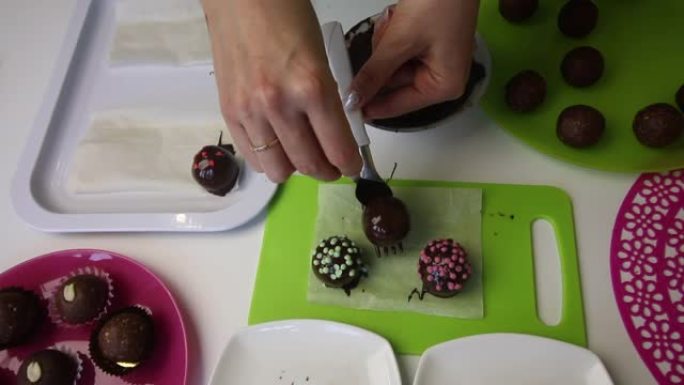 一个女人在表面上放了一个巧克力海绵球。做一个土豆蛋糕。盘子旁边是蛋糕坯料，液体巧克力和彩色洒。