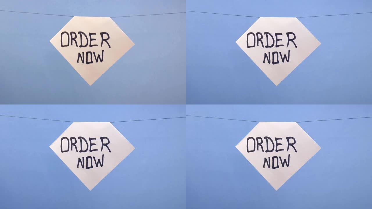 一名男子在蓝色背景上悬挂一张白纸，上面刻有黑色铭文 “order now”